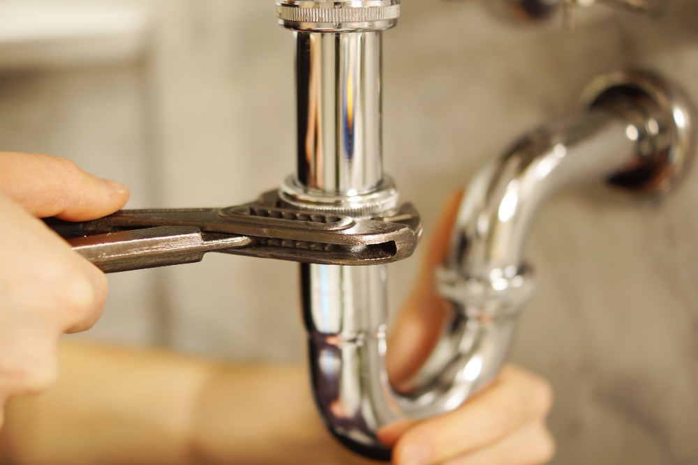 A plumber uses a wrench to repair chrome pipes. Plumbing repair work with tools.