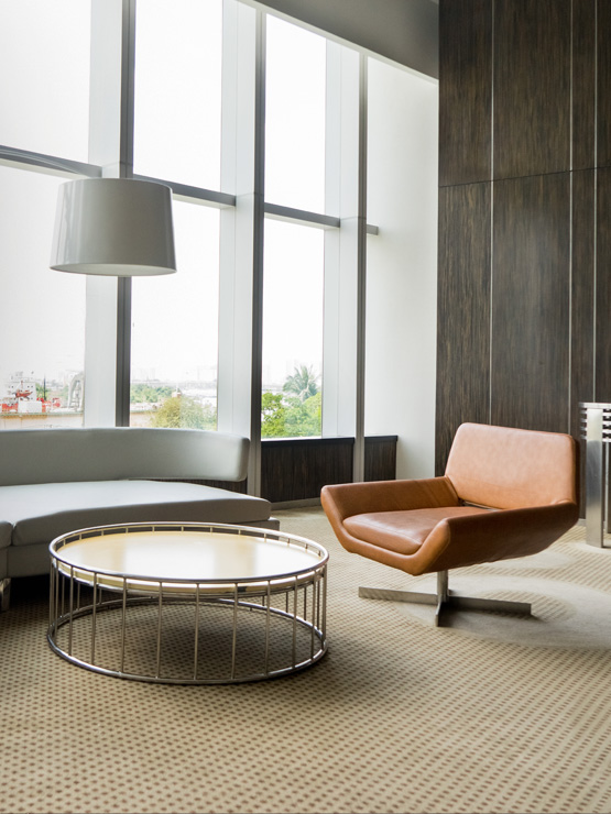 Modern living room with leather chair, round coffee table, large windows, and neutral carpet.