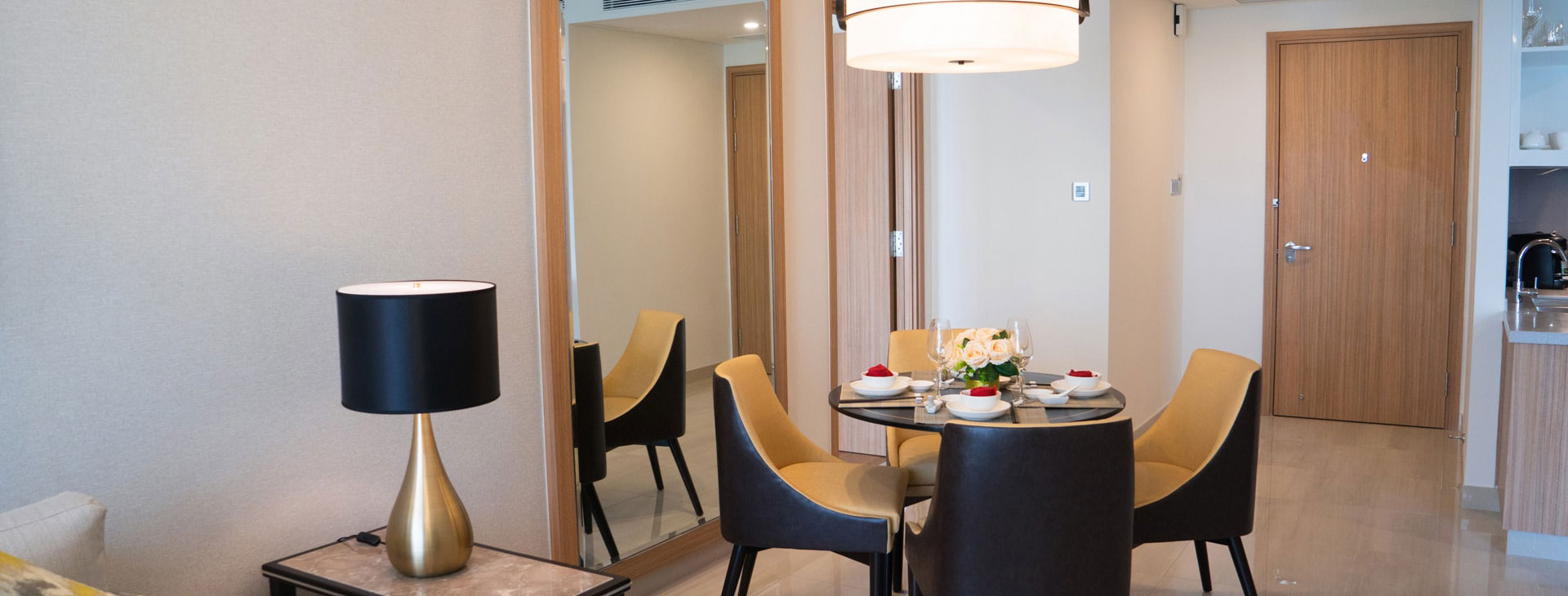 Interior shot of a modern dining room with a round table set for four, chairs, a lamp, & a mirror.