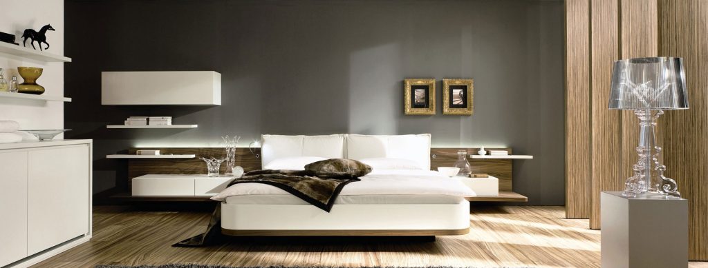 Modern bedroom with minimalist design featuring a bed, floating shelves, artwork, and a decorative lamp on a side table.